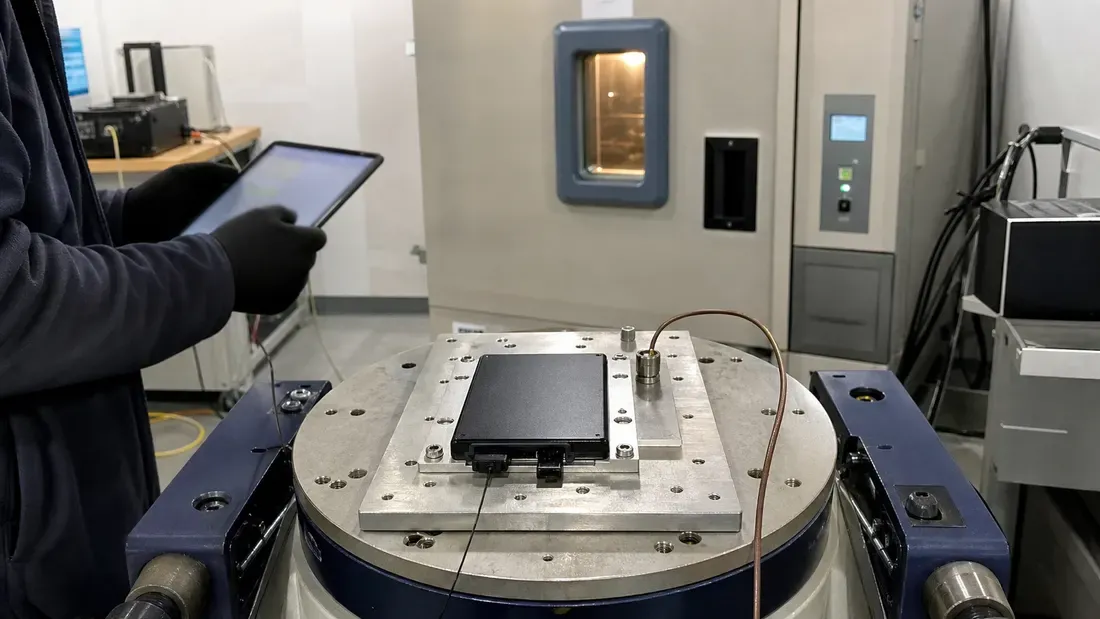 Industrial SSD mounted on an instrumented vibration fixture beside an environmental chamber