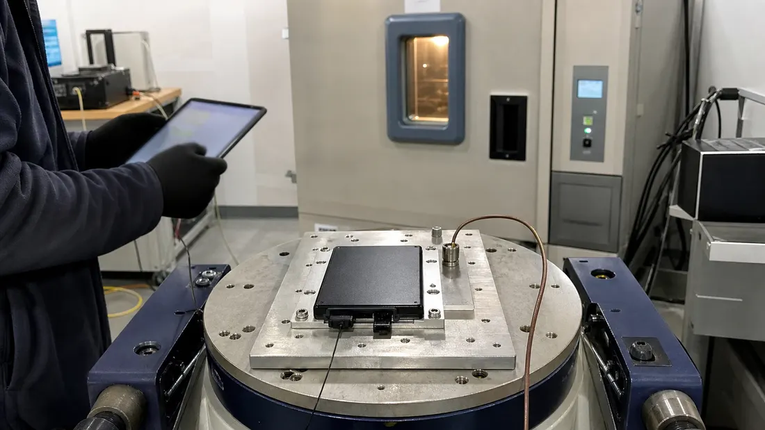 Industrial SSD mounted on an instrumented vibration fixture beside an environmental chamber